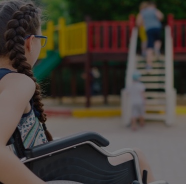 A child in a wheelchair with children and playground in the background