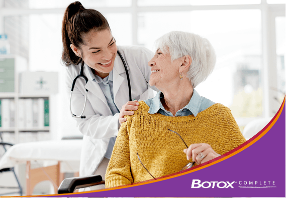 A doctor in a lab coat with a stethoscope smiling at a patient who is holding glasses